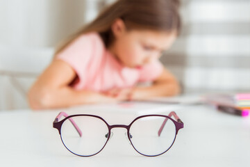 Little girl is reading school textbooks in a blurry image. Glasses for vision in focus. Poor vision...
