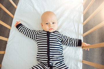 Cute baby in wooden bed at home, top view
