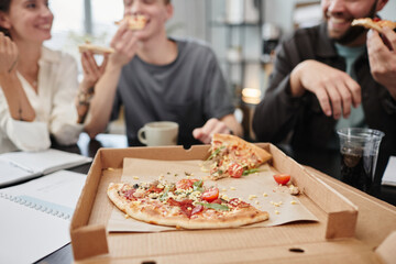 Close-up of fresh pizza in the opened box with business people having lunch at the table in the background