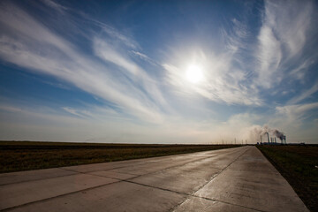 Concrete slabs road and blue sky with clouds. Silhouette of power plant on horizon. Pavlodar, Kazakhstan.