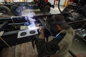 Welder in protective mask and work suit welding metal part of vehicle. Uralsk, Kazakhstan