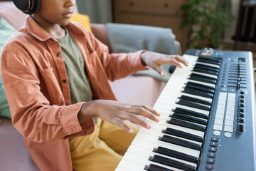 Hands of biracial schoolboy in casualwear over keys of music keyboard during lesson in home...