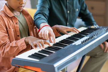 Hand of young teacher of music pointing at one of keys of piano keyboard during lesson in home...