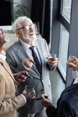 high angle view of senior multiethnic business partners with cigars and glasses of whiskey laughing in office