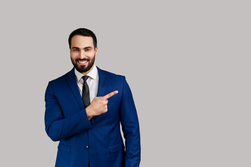 Positive bearded man pointing finger away with toothy smile on face, empty space for your...