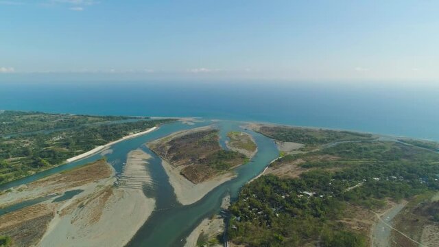 Aerial view of wide river flowing into the blue sea. Tropical landscape with sandy coast and river among farmer fields flowing into the blue ocean.