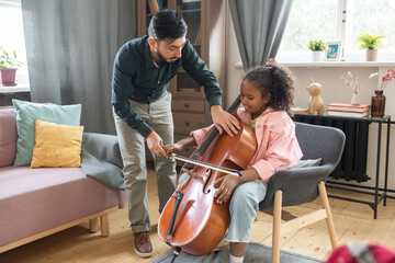 Young man bending over cute diligent schoolgirl with cello while teaching her how to play musical instrument © pressmaster