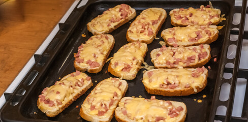 Oven-baked sandwiches with bread, sausage and cheese close-up on a black baking sheet
