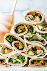 A leaning pile of fresh deli wraps with a glass of sparkling juice in behind.