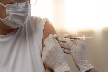 Hand staff nurse wearing rubber gloves using a syringe is giving vaccinations covid-19 to an...
