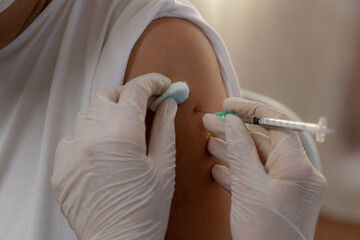 Close-up shot of a hand nurse wearing rubber gloves using a syringe is vaccinating covid-19 to an elderly woman.