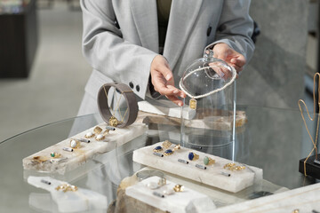 Hands of young elegant woman taking pearl necklace on hanger while going to show it to consumer of jewelry boutique