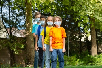 Group of schoolchildren in masks walking together on the park