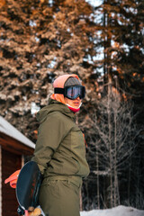 Fototapeta na wymiar Winter sports. Portrait of a snowboarding girl against the background of a wooden house and a winter forest.
