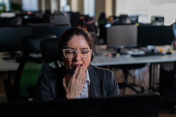 Business woman yawns at her desk in the office.