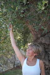 Frau schaut sich Oliven an einem Olivenbaum an und lächelt