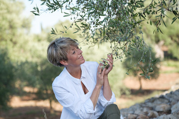 Frau berührt Oliven an einem Olivenbaum und lächelt