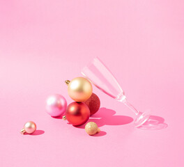 Christmas balls with a glass on a pink background. New year or Christmas eve party concept.