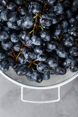 Sweet black grapes in a metal bowl on a dark textured background.