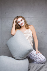 Fototapeta premium The girl sits on the sofa wearing a cosmetic mask.