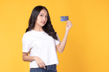 Portrait of a happy young asian woman wearing white shirt holding bank card, credit card isolated on yellow background. Business online shopping concept.