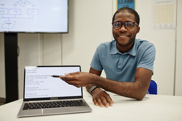 Portrait of young black teacher pointing at laptop screen in coding class for children, copy space