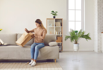 Smiling young woman sit on couch do unpacking at home shopping online. Happy girl client or...