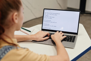 High angle portrait of teenage girl using laptop and coding in programming school for children,...