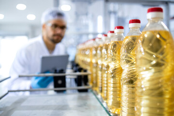 Bottled vegetable oil production in food factory and worker in white coat with hairnet controlling process.