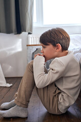 Teen boy sitting on floor near bed, Offended upset boy teenageralone. Schoolboy torturing of...