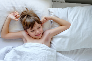 Obraz na płótnie Canvas Sleepy happy child lying in a bed, waking up in the morning. Relax time. Morning time. Morning in bedroom. Bed time. Handsome caucasian teen boy on bed in light interior, top view portrait