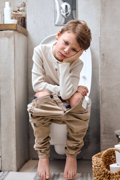 School boy is sitting on toilet with suffering from constipation or hemorrhoid. caucasian kid is on wc seat, bored and tired, have rest relaxed. hygiene, health care concept