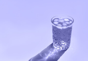 Beautiful crystal glass casts long shadow from sunlight. Toned in trendy color of year 2022. Minimal creative composition with copy space. Summer drinks concept.