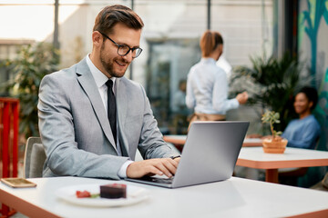 Happy businessman types e-mail while working on laptop in cafe.