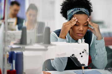 Exhausted black seamstress has headache while working on production line at textile factory.
