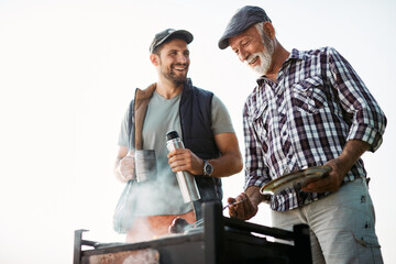 Below view of happy father and son prepare food on barbecue grill in nature.