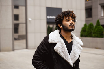 Indian man in jacket and earphone standing on urban street 