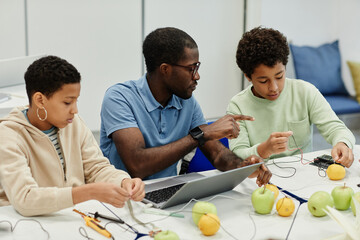 Portrait of young African-American teacher working on science experiments with diverse group of children