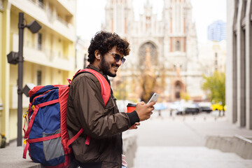 Indian tourist with backpack using cellphone in city 