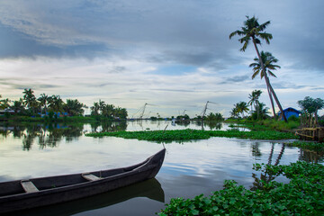 Naklejka na ściany i meble Wooden fishing boat on river - Backwaters photography, typical landscape with palm trees and old hut, Kerala Backwaters, Kerala backwaters photography during day time Kadamakkudy Kerala