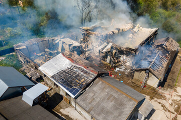 Aerial view of ruined building on fire with collapsed roof and rising dark smoke
