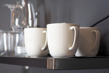 three white mugs stand on a wooden shelf in the kitchen. side view