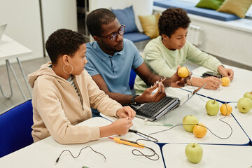 High angle portrait of young African-American teacher working on science experiments with diverse...