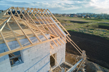 Obraz premium Aerial view of unfinished frame of private house with aerated lightweight concrete walls and wooden roof frame under construction