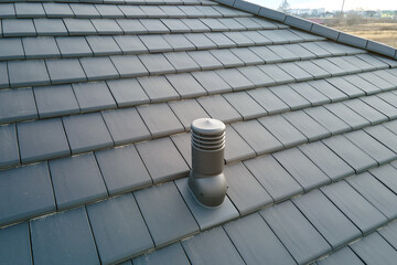 Closeup of ventilation pipe on house roof top covered with ceramic shingles. Tiled covering of...