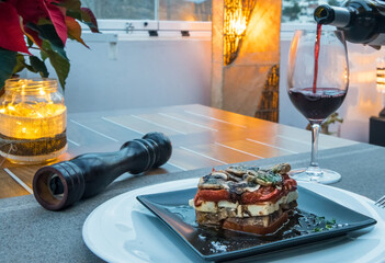 Timbal o torre templada de berenjenas , queso y pimientos rojos con copa de vino tinto.
