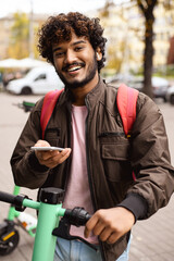 Smiling indian man using app on smartphone near public electric scooter on street  © Dmytro Hai