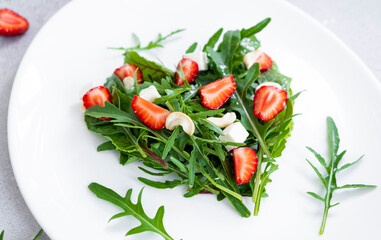 Romantic salad of strawberry with mix of herbs, arugula, spinach leaves, feta cheese and cashew nuts in heart shape on white plate. Romantic meal for St Valentine Day celebration.