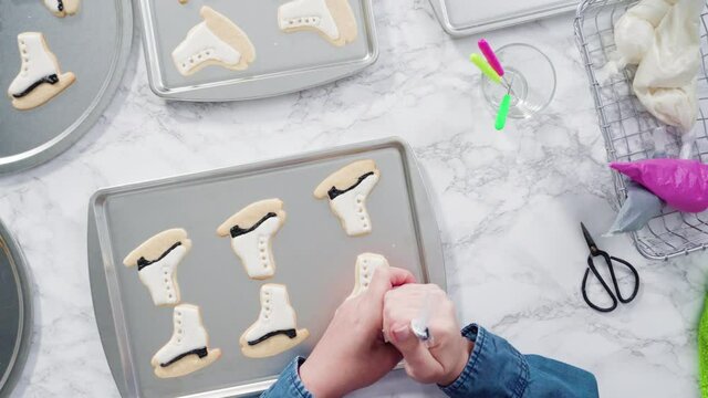 Flat lay. Decorating ice skate shaped sugar cookies with black color royal icing.