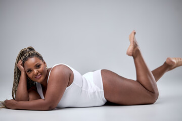 Fototapeta na wymiar Beautiful young plus size young overwight woman wearing white bodysuit posing over isolated white background with a happy and cool smile on face, lying on floor. Lucky person. body positive concept